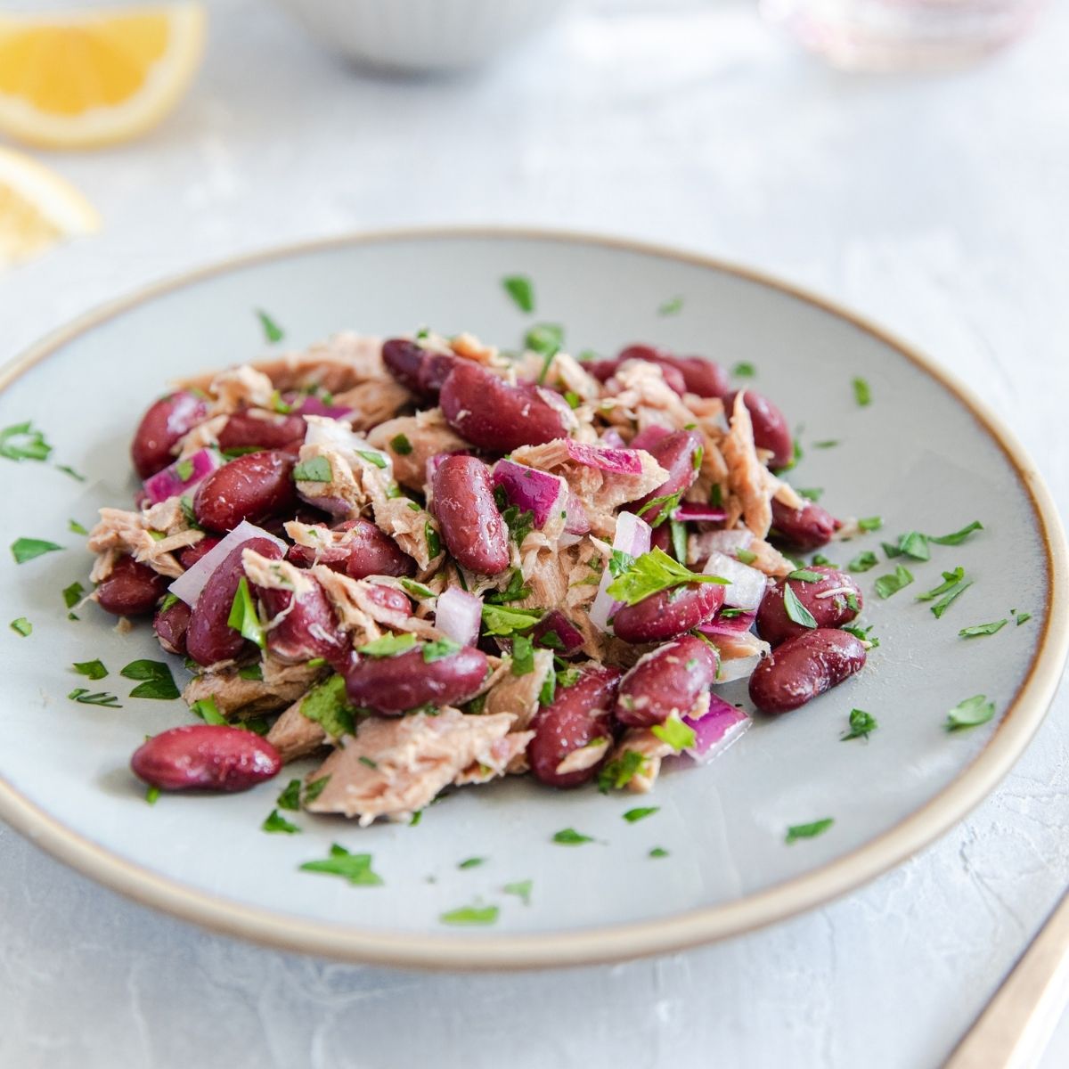 Tuna and organic kidney bean salad on a white plate with lemon wedge and parsley garnish