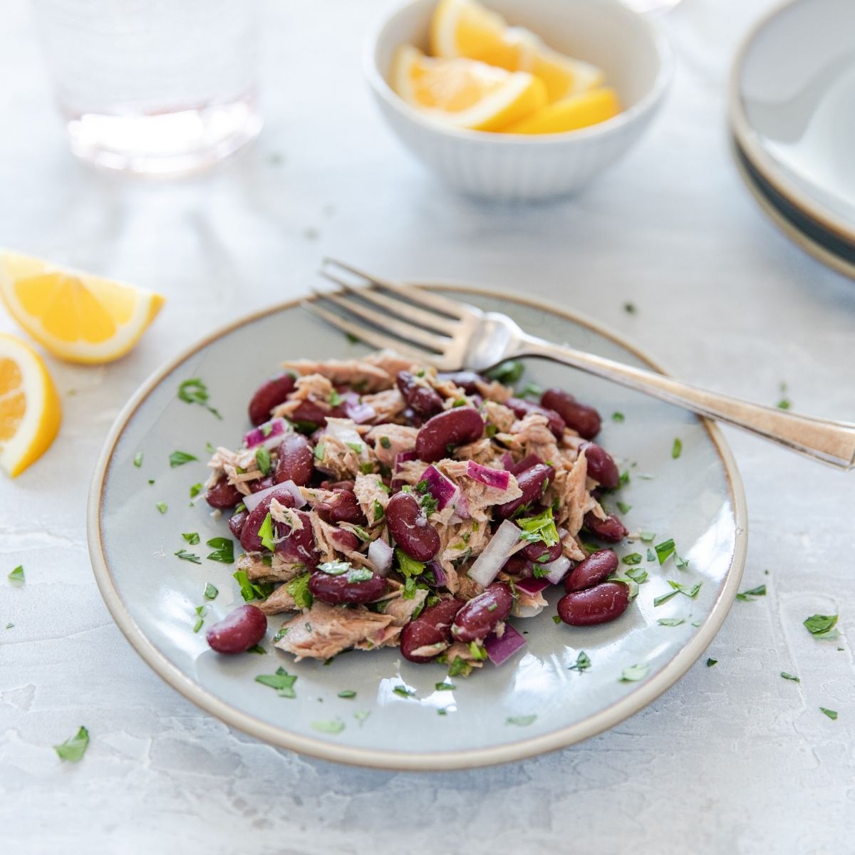 Tuna and organic kidney bean salad plated for serving with lemon wedges and a fork on a light tabletop