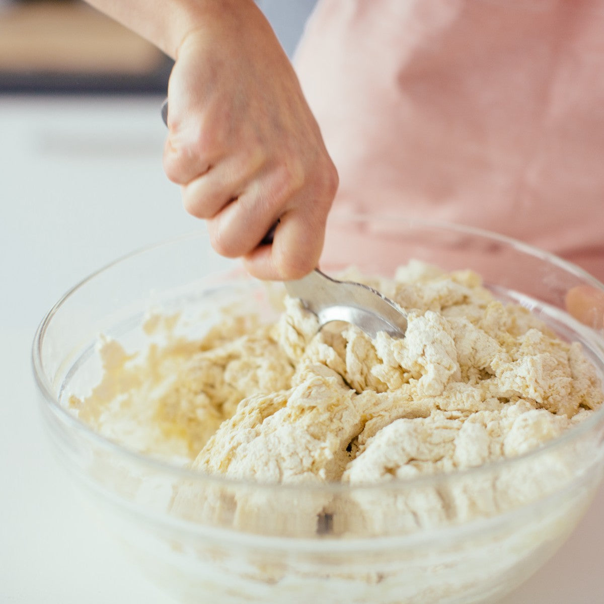 Close up of kneading tool stirring Einkorn dough in a glass bowl showcasing the tool mixing action with a hand on the handle