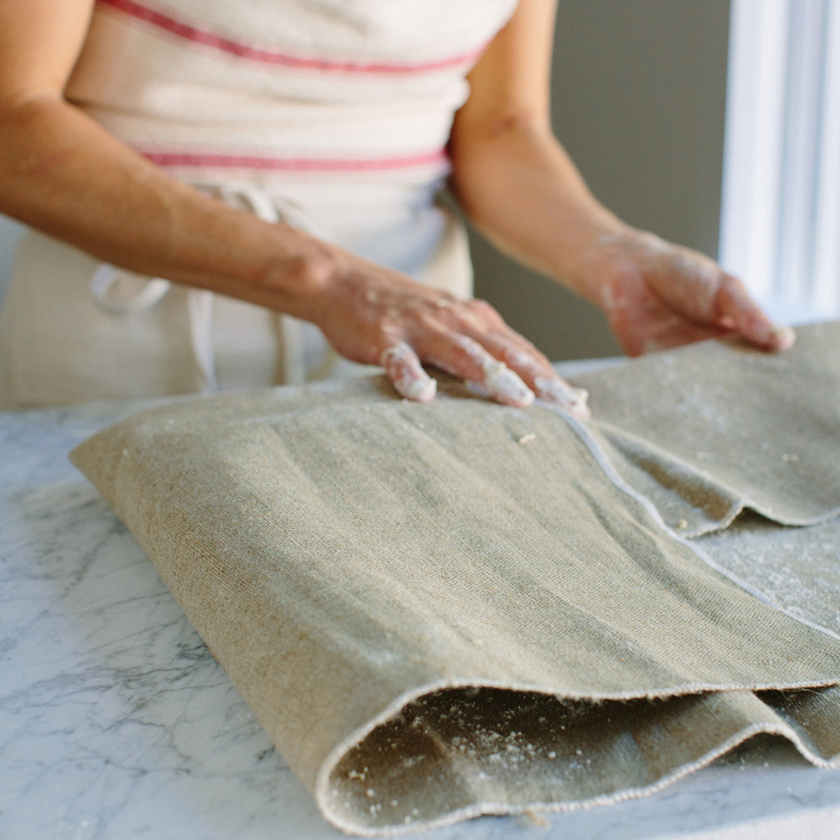 Top-down view of Jovial Linen Couche showcasing natural unbleached linen texture and folded length on marble countertop