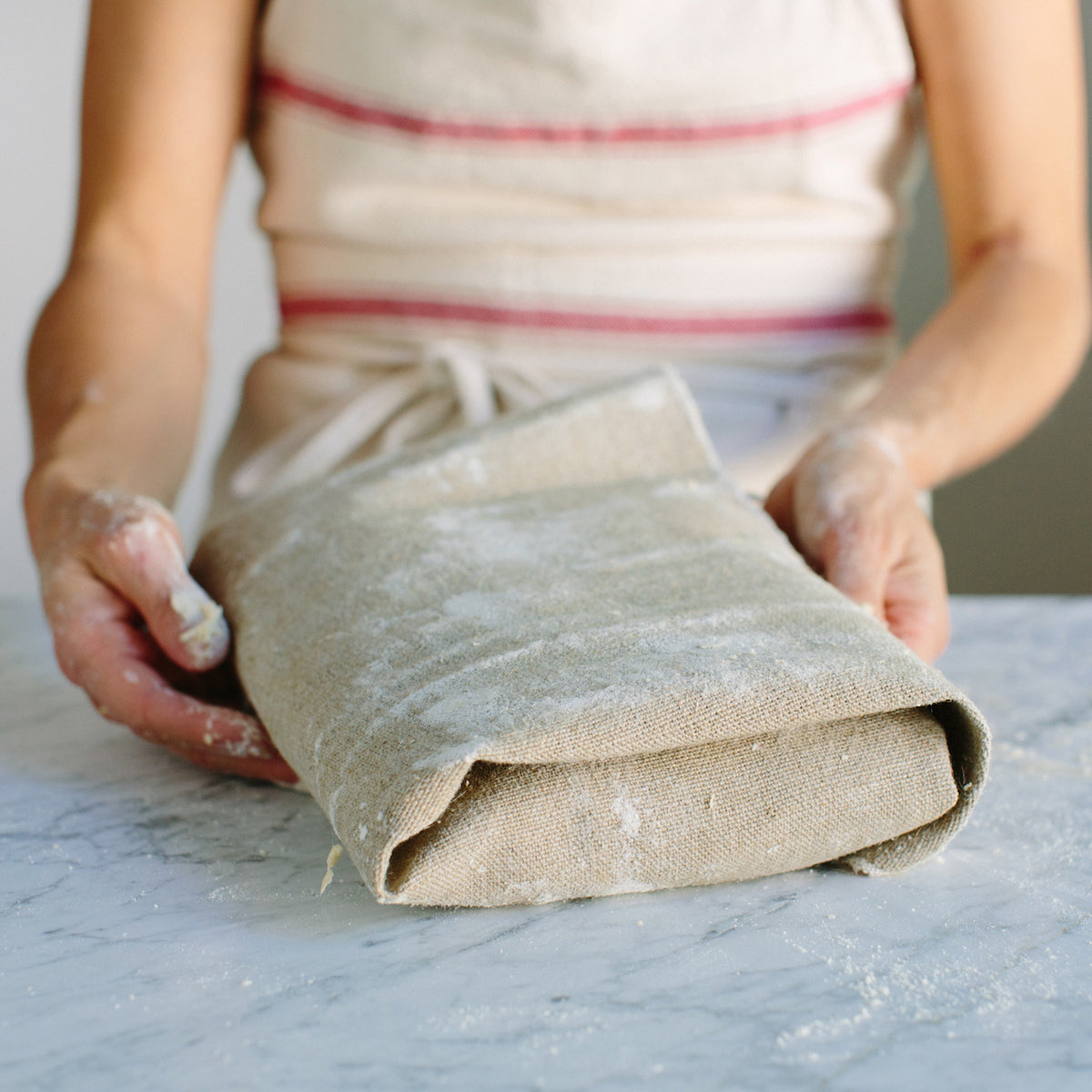 Close-up of linen couche showcasing folded natural flax texture with light flour dusting on a wooden countertop