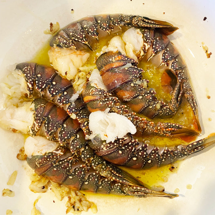 Lobster tails simmering in garlic-butter sauce in a white pan