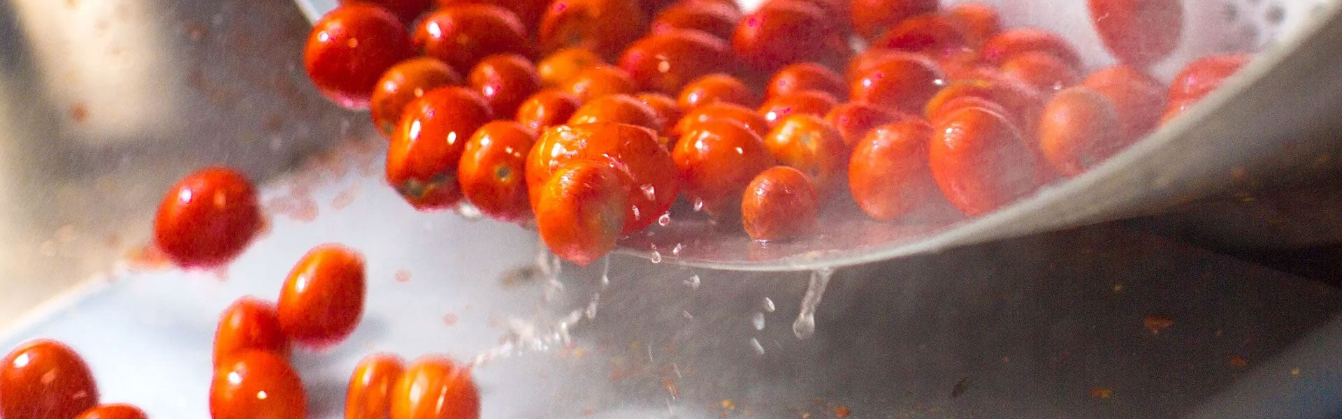 Cherry tomatoes being drained from a metal spoon with water droplets falling