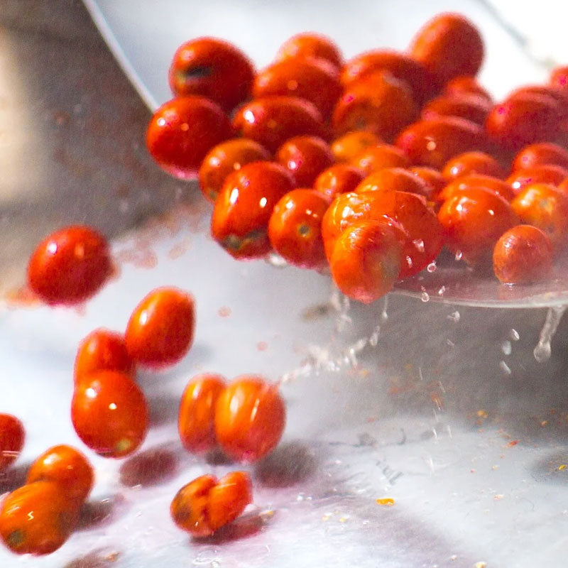 Cherry tomatoes draining from a slotted spoon with water droplets