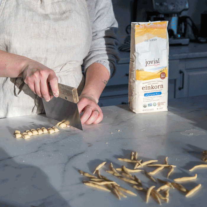 Person cutting hand-rolled egg-free einkorn pasta into trofie on a marble counter with Jovial einkorn flour bag nearby