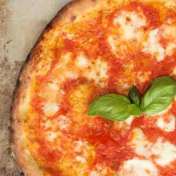 Close-up top view of Neapolitan Margherita pizza with blistered crust, tomato sauce, melted mozzarella, and fresh basil on a stone surface