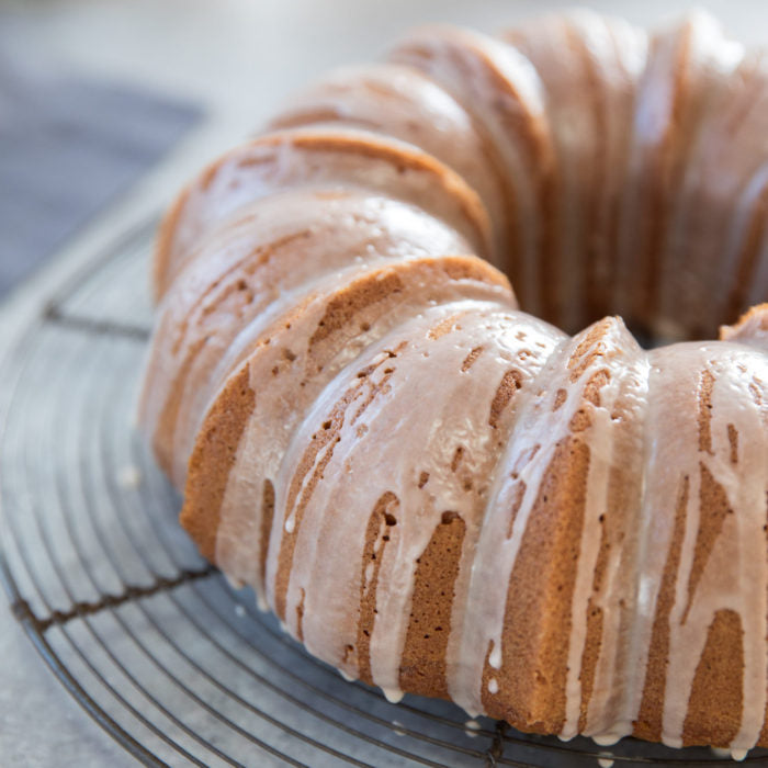 Close-up side view of an Einkorn pumpkin spice bundt cake with white glaze dripping over ridged sides on a wire cooling rack