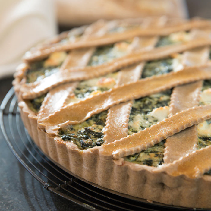 Close-up of einkorn spinach and ricotta pie with lattice crust showing ricotta pockets and wilted spinach on a cooling rack