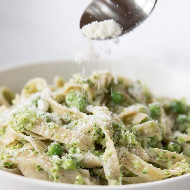 Close up of creamy broccoli tagliatelle with peas topped with grated cheese being sprinkled from a spoon