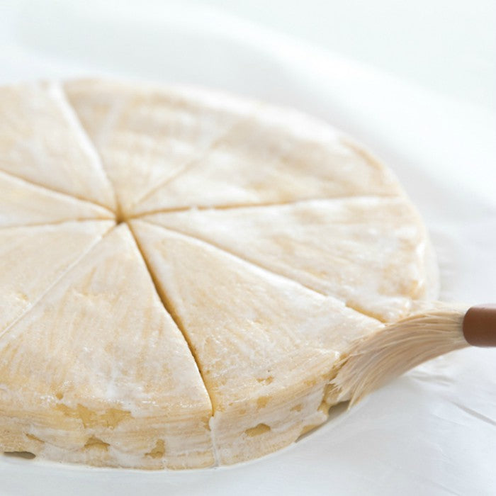 Einkorn cinnamon scone dough cut into eight wedges being brushed with a pastry brush on parchment