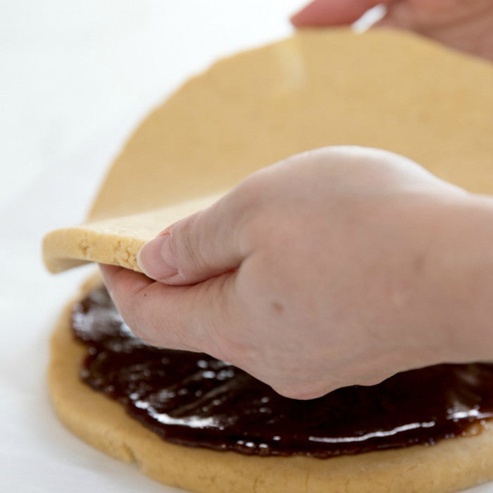 Hands placing a round dough layer over spiced filling for Einkorn cinnamon scones