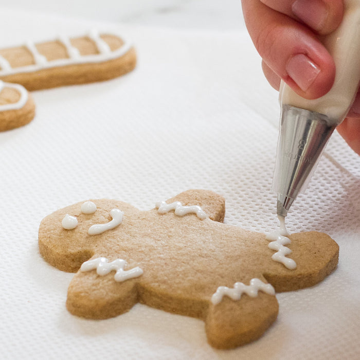 Close up of an Einkorn sugar cookie in a gingerbread shape being decorated with white icing on parchment paper