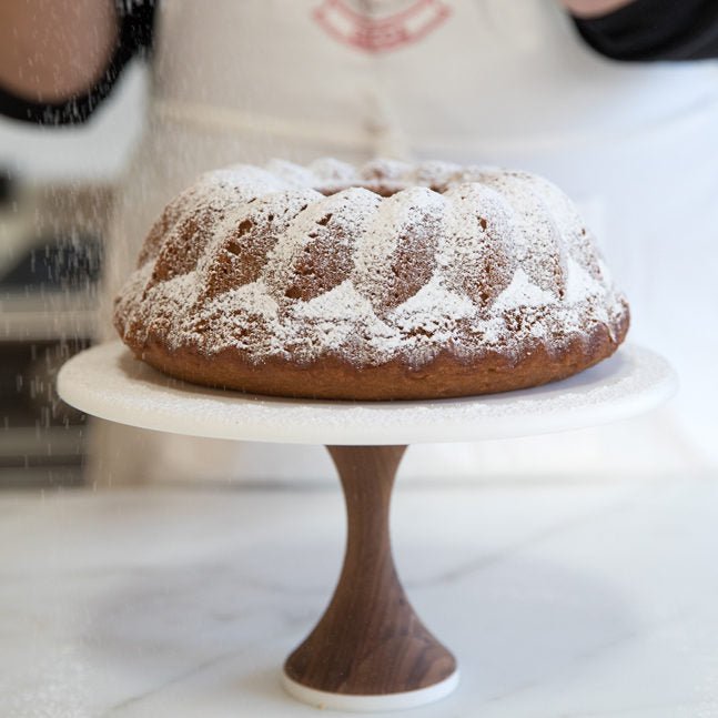 Side view of Einkorn pumpkin spice bundt cake dusted with powdered sugar on a wood cake stand, blurred kitchen background
