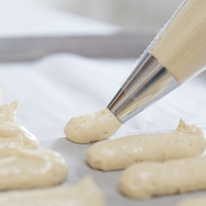 Pastry bag piping einkorn ladyfinger batter onto parchment for tiramisu