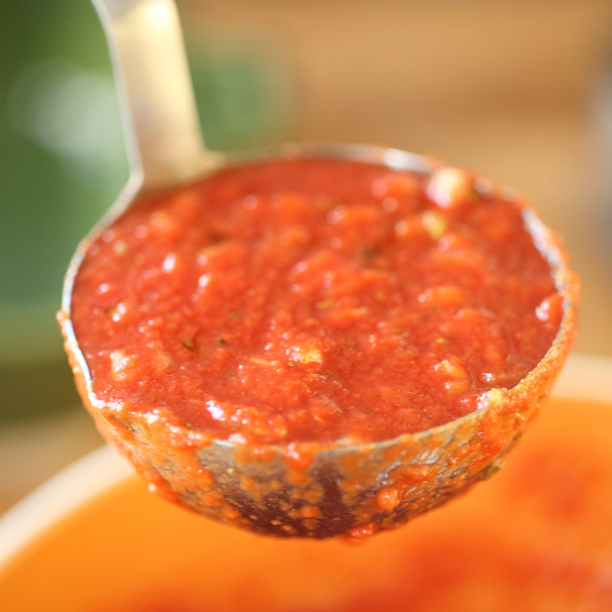 Close-up of Organic Italian crushed tomatoes in a ladle showcasing chunky texture over a pot