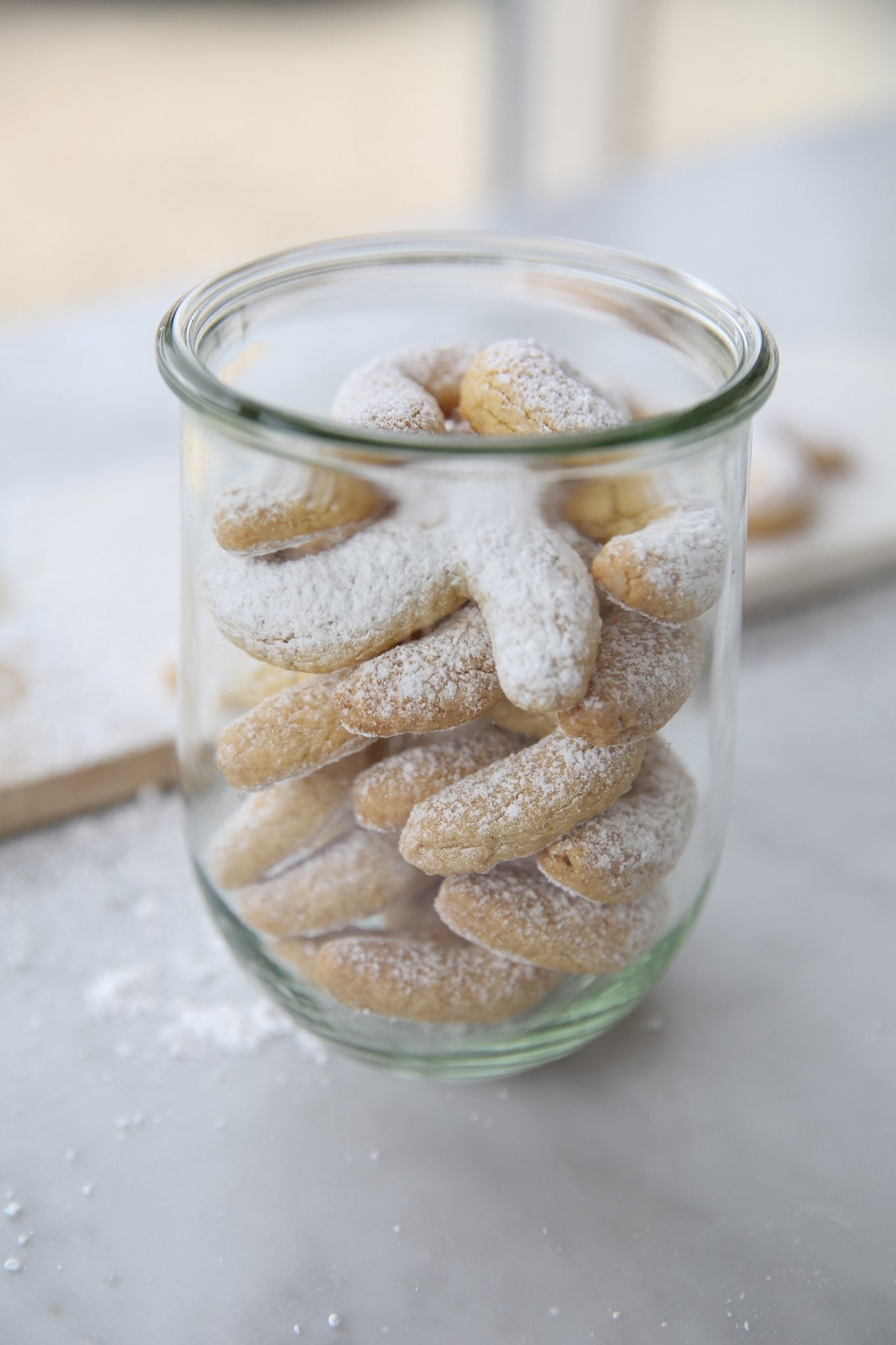 Front view of Einkorn Italian shortbread cookies stacked in a glass jar, dusted with powdered sugar on a marble surface