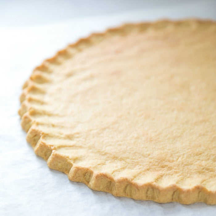 Close-up of a 12-inch Einkorn sugar cookie crust with crimped crimped edge on parchment paper