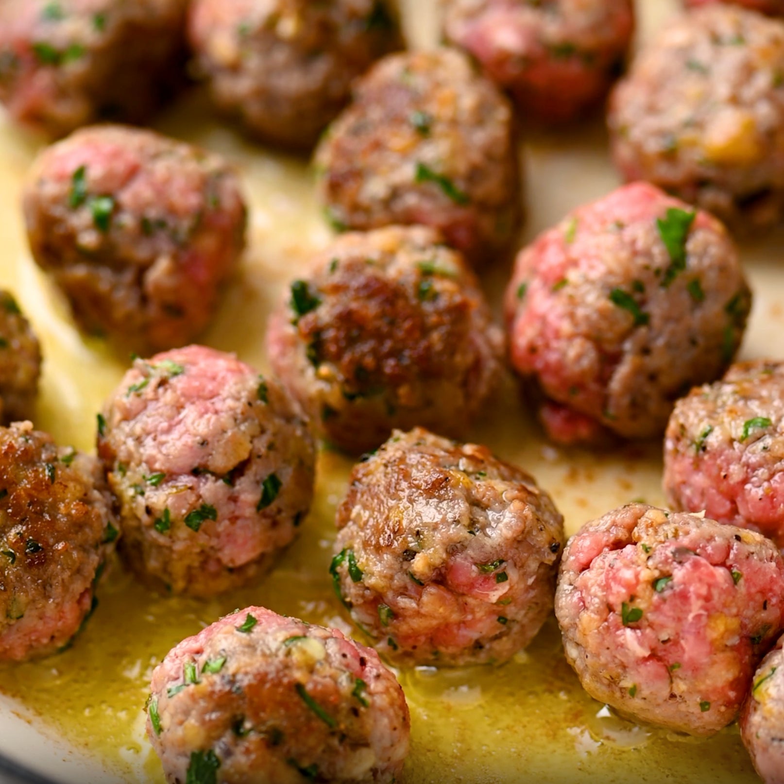 Italian-style mini meatballs browning in a skillet with parsley and cooking juices