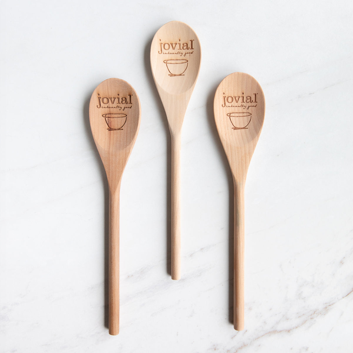 Overhead view of three hand made 12-inch birch wooden spoons engraved with the Jovial logo on a white marble background