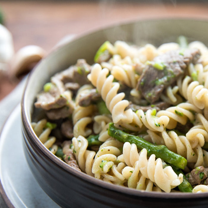 Close-up of gluten-free fusilli with steak, asparagus, and broccoli in a ceramic bowl showing spiral pasta