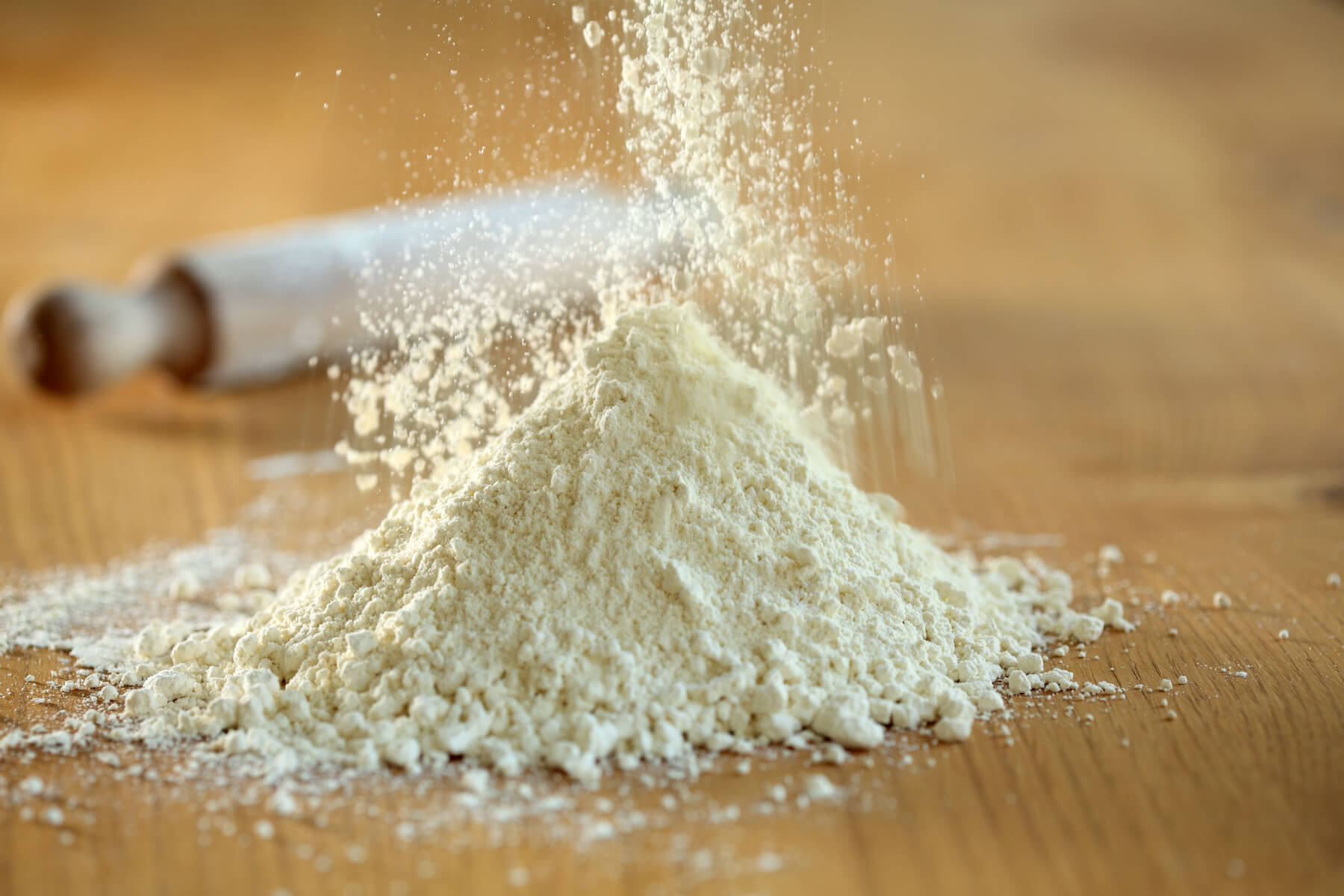 Close-up of organic einkorn flour being sifted into a small mound on a wooden board with a rolling pin blurred behind