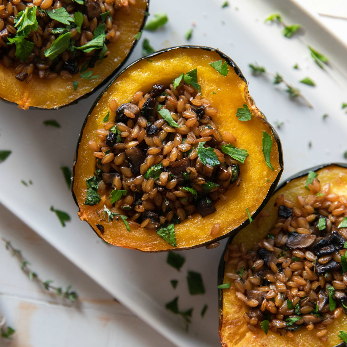 Roasted acorn squash halves stuffed with cooked einkorn wheat berries and sautéed mushrooms, garnished with chopped parsley on a white platter