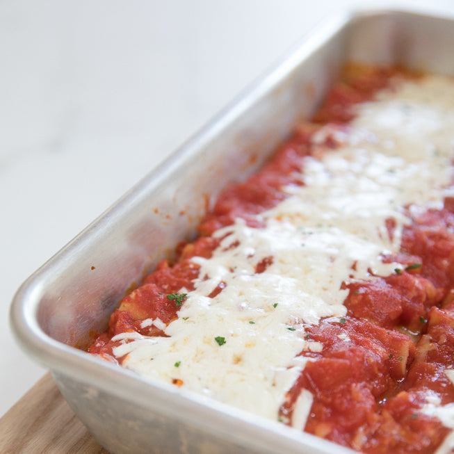 Angled close-up of gluten-free turkey and spinach manicotti in a metal baking pan topped with melted cheese and tomato sauce