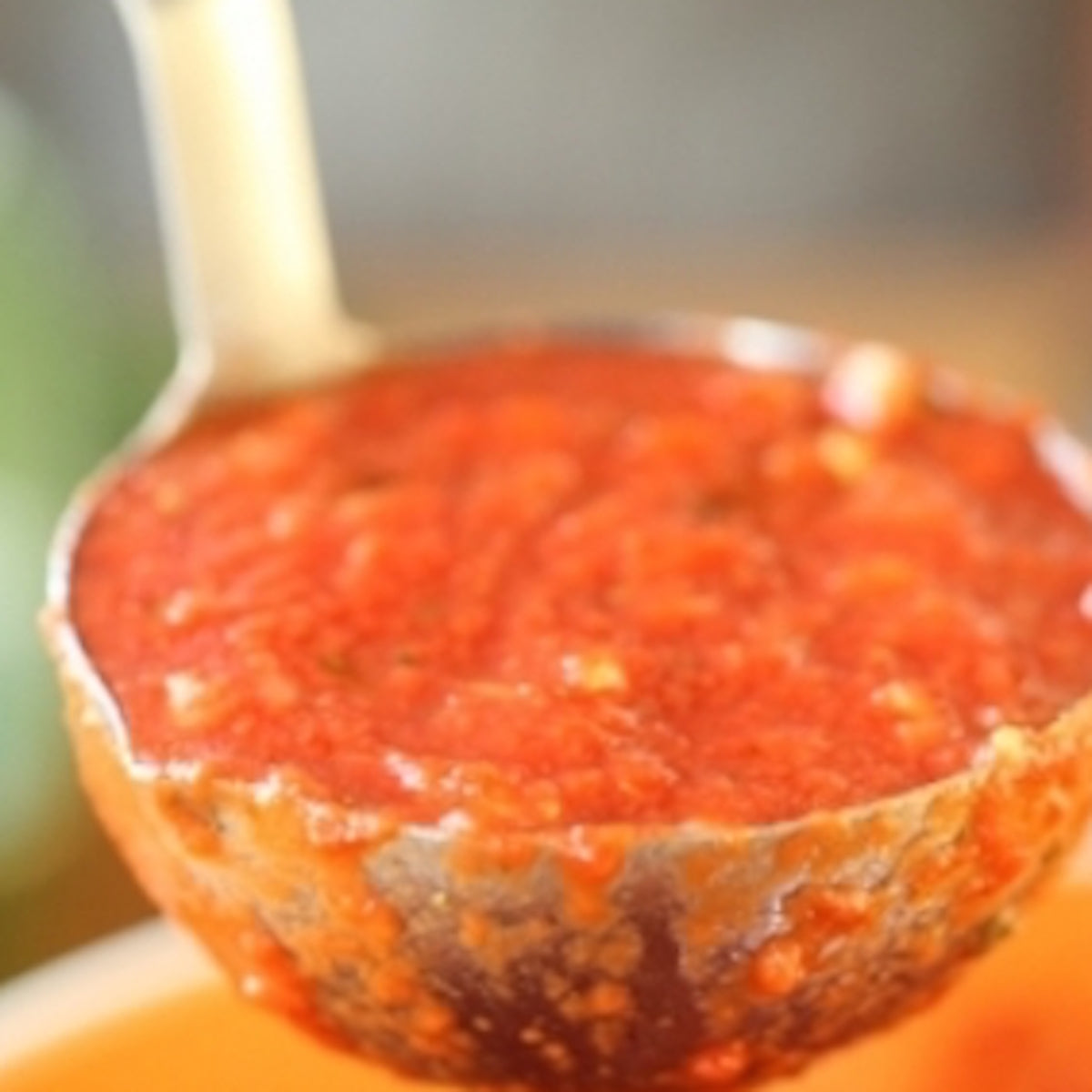 Ladle pouring chunky tomato sauce into an orange bowl