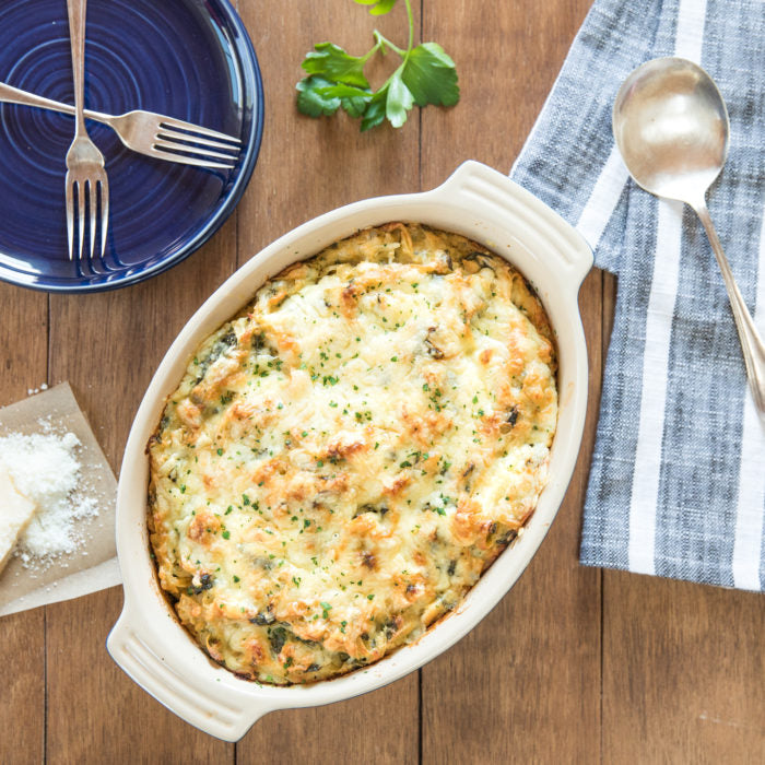 Top-down view of gluten-free tuna casserole in oval dish topped with golden cheese and parsley on a wooden table
