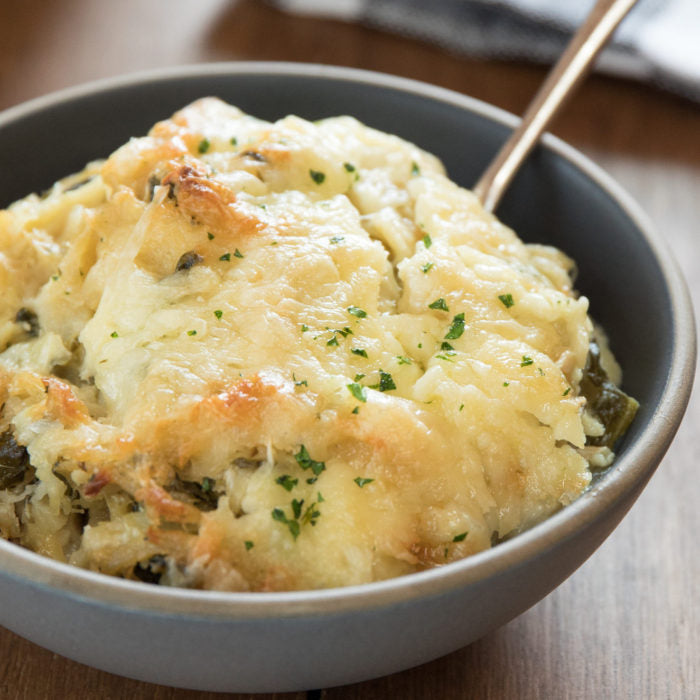 Close-up of gluten-free tuna casserole in a bowl showcasing golden melted cheese topping and chopped parsley on a wooden table