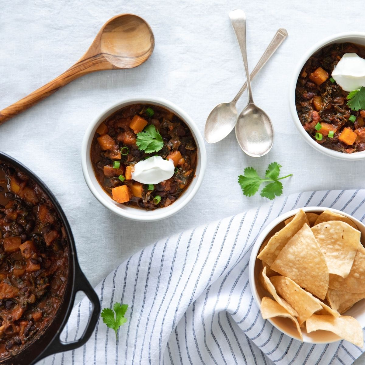 Bowl of vegetarian chili made with organic borlotti beans served with tortilla chips and spoons on a striped cloth