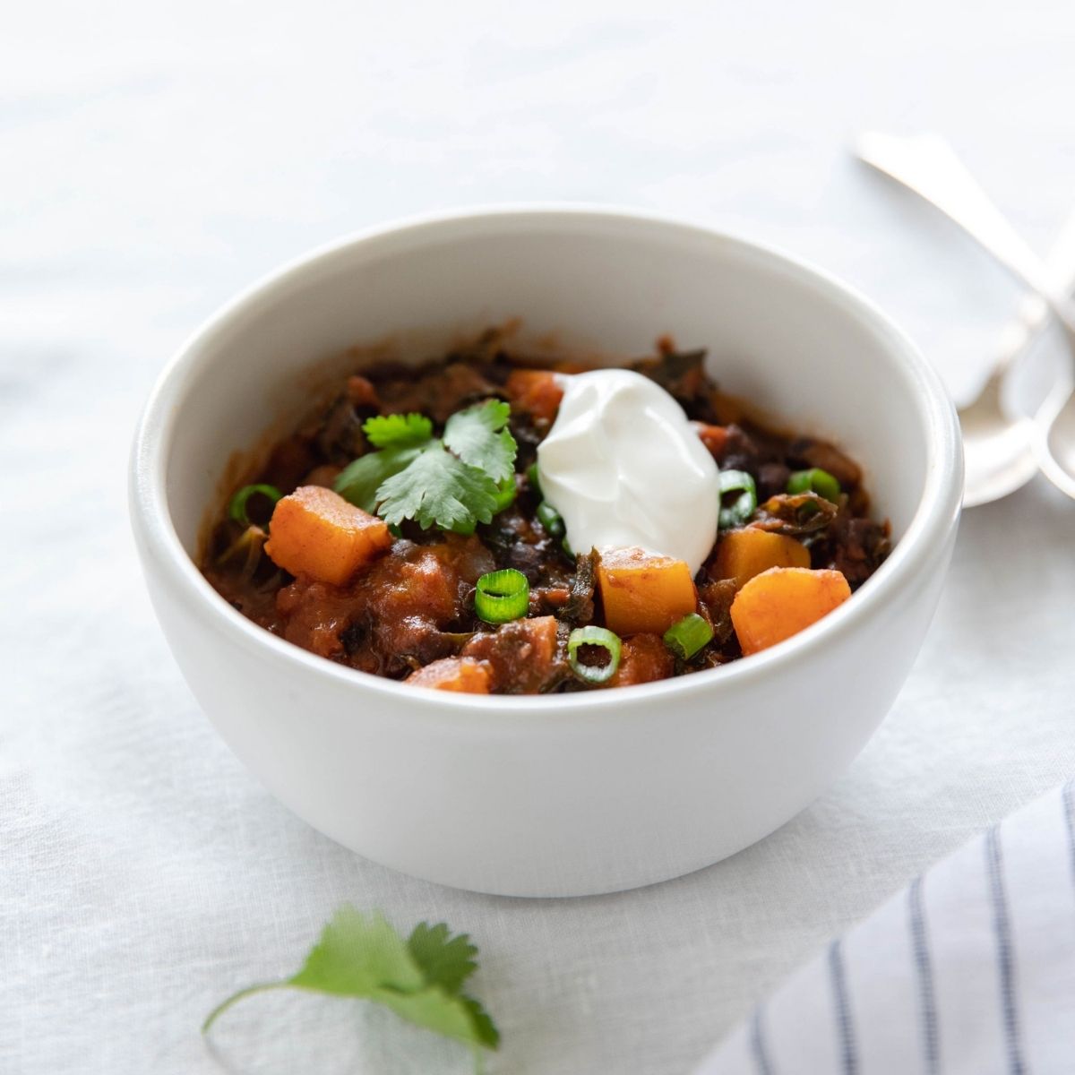 Bowl of vegetarian chili with organic borlotti beans, diced carrots and greens, topped with sour cream, cilantro, and sliced scallions