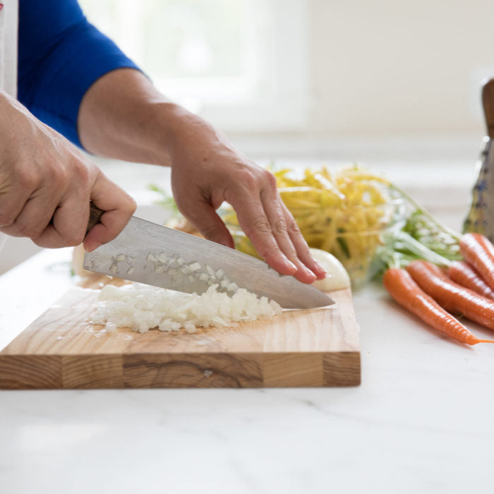 Hands chopping an onion on a wooden cutting board with yellow wax beans and carrots nearby