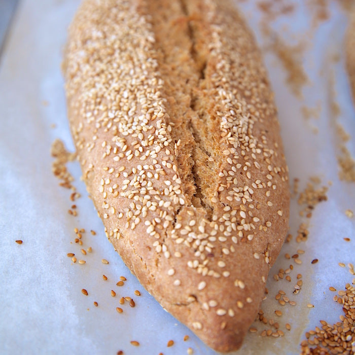 Top-down close-up of crusty Einkorn Italian bread loaf with sesame seeds on parchment paper