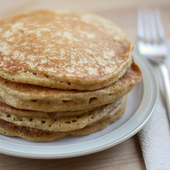 Stack of golden-brown pancakes made with Jovial organic einkorn whole wheat flour on a white plate with a fork and napkin
