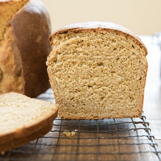 Sliced whole-grain einkorn loaf on a cooling rack, showing a dense golden crumb and crust