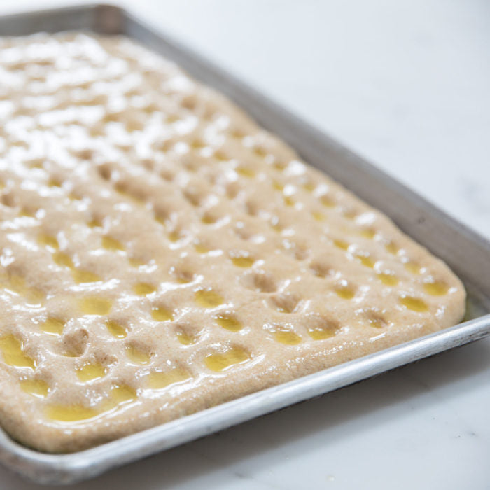 Close-up of Einkorn whole wheat focaccia dough in a rimmed baking pan with finger dimples filled with olive oil