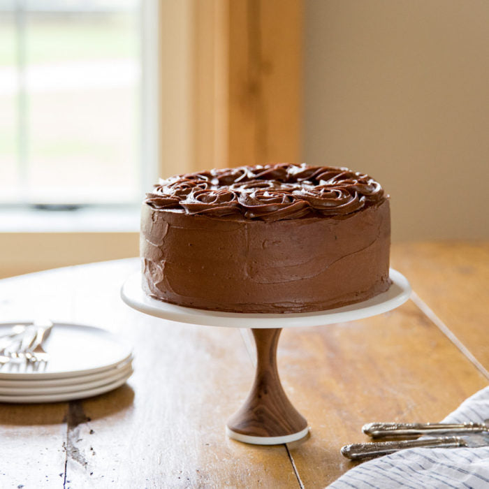 Side view of Einkorn yellow layer cake with chocolate buttercream rosettes on a wood cake stand on a sunlit wooden table