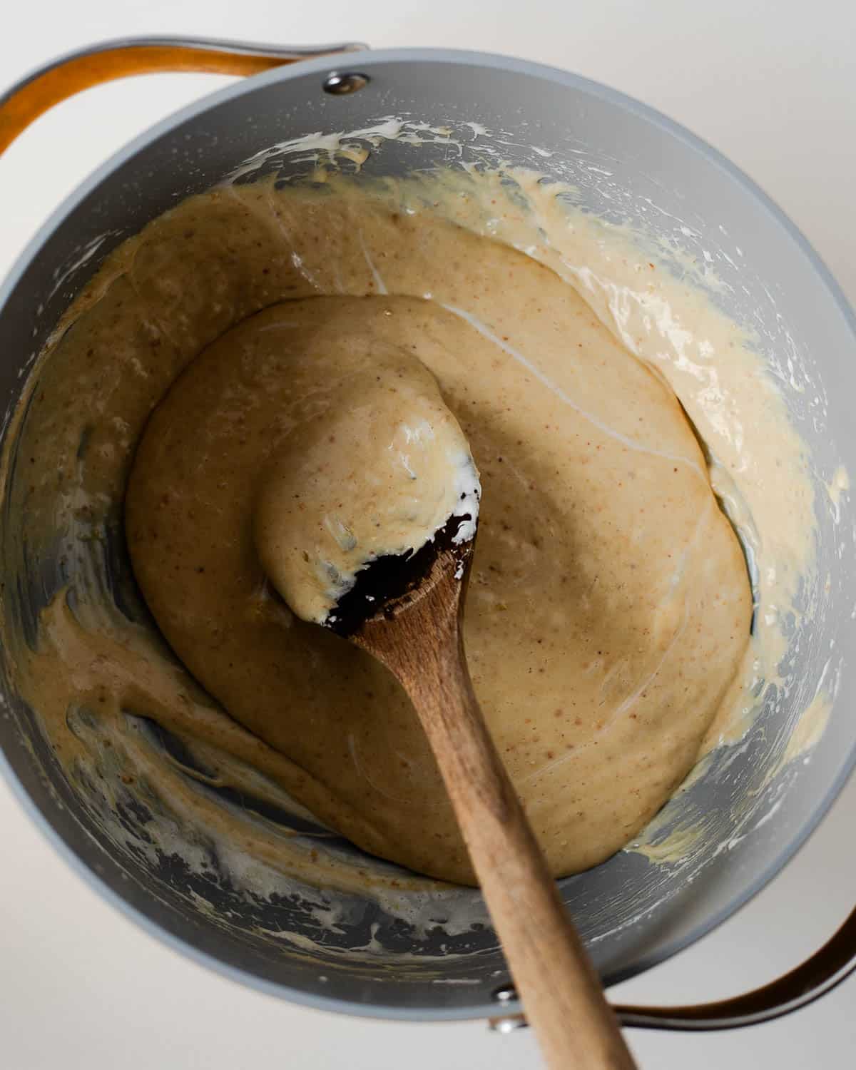 Melted mini marshmallows and peanut butter mixture in a large pot being stirred with a wooden spoon.