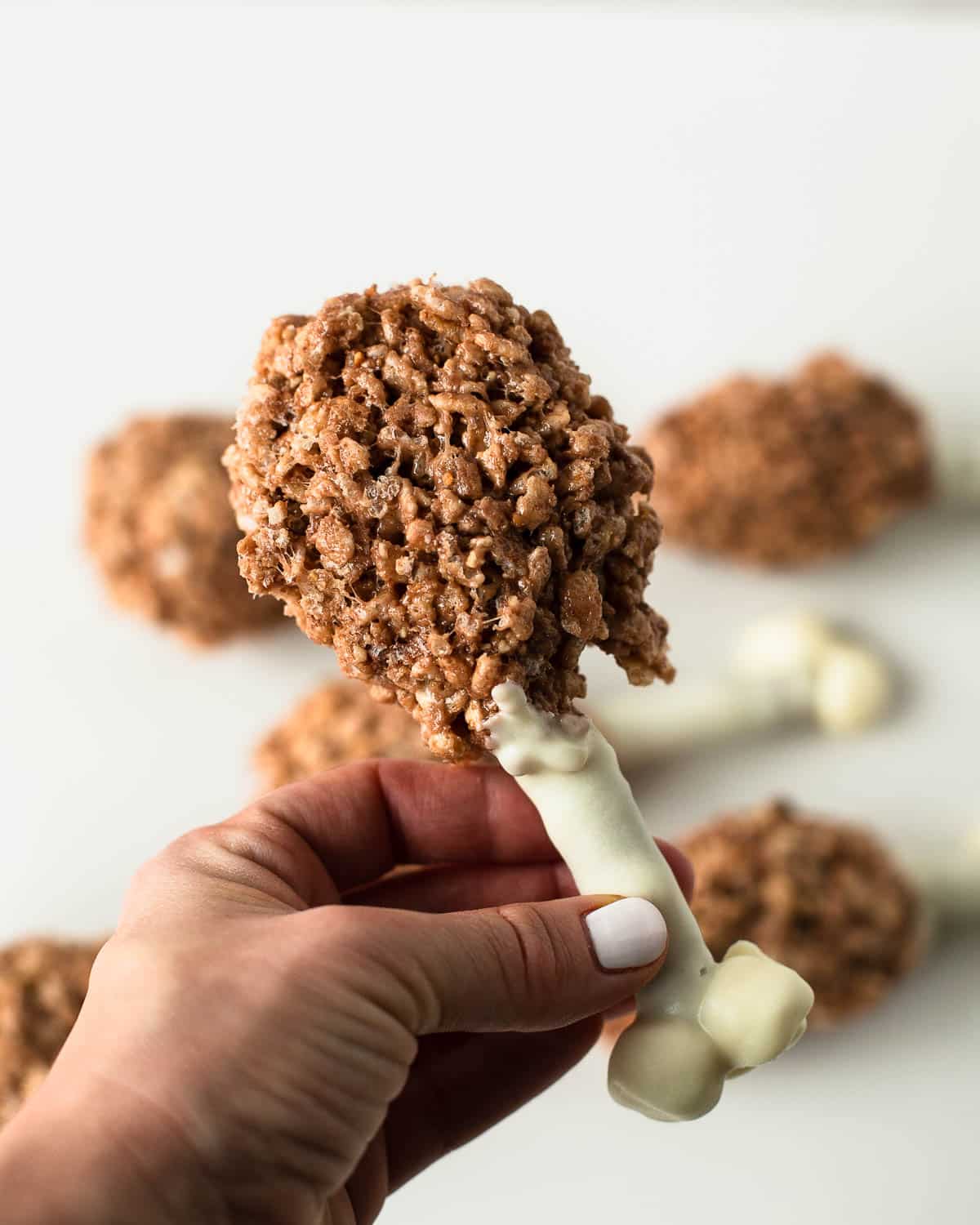 Hand holding a finished Rice Krispie turkey leg treat with white chocolate pretzel bone.