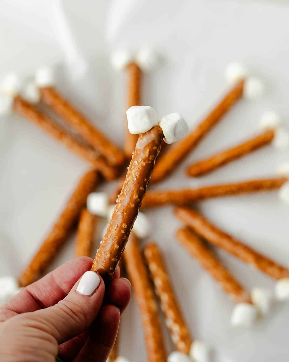 hand holding pretzel rod bones with mini marshmallow ends, prepped to make Rice Krispies turkey drumsticks