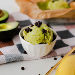 Close-up of dairy-free avocado banana ice cream in a bowl topped with mini chocolate chips, styled with fresh avocado and banana in the background