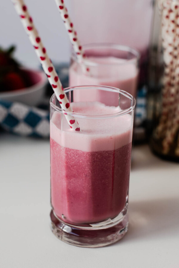 Close-up of a glass filled with creamy pink dairy-free strawberry milk, heart straw tucked in for sipping.