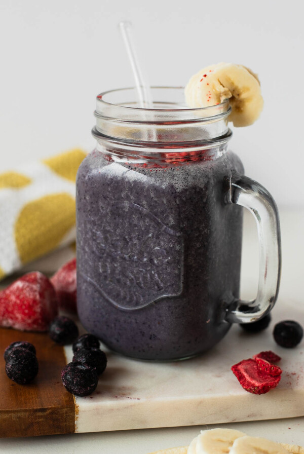 Mason jar of blueberry-strawberry egg white protein shake with banana garnish and glass straw.
