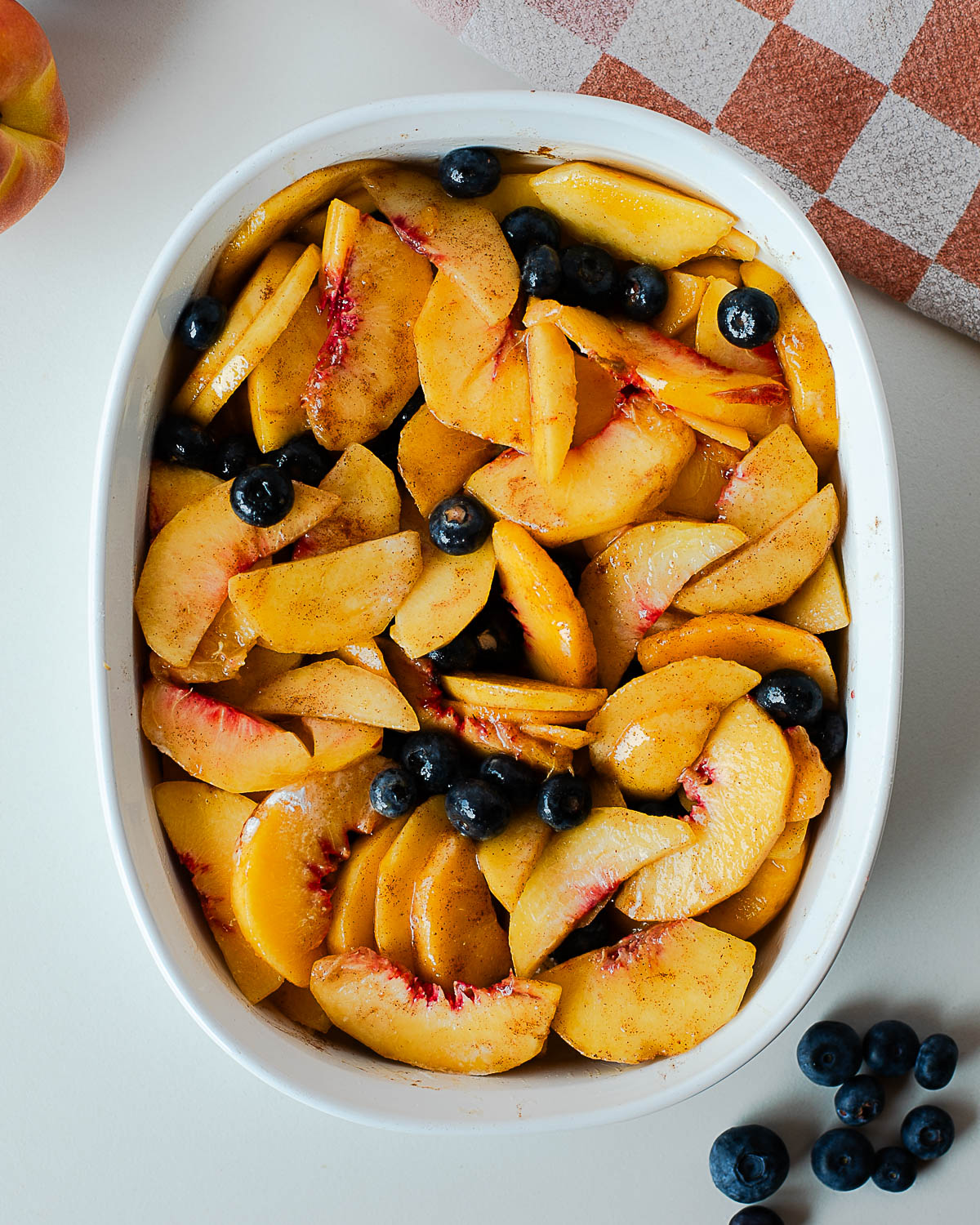 Sliced peaches and blueberries tossed with cinnamon in a white baking dish.