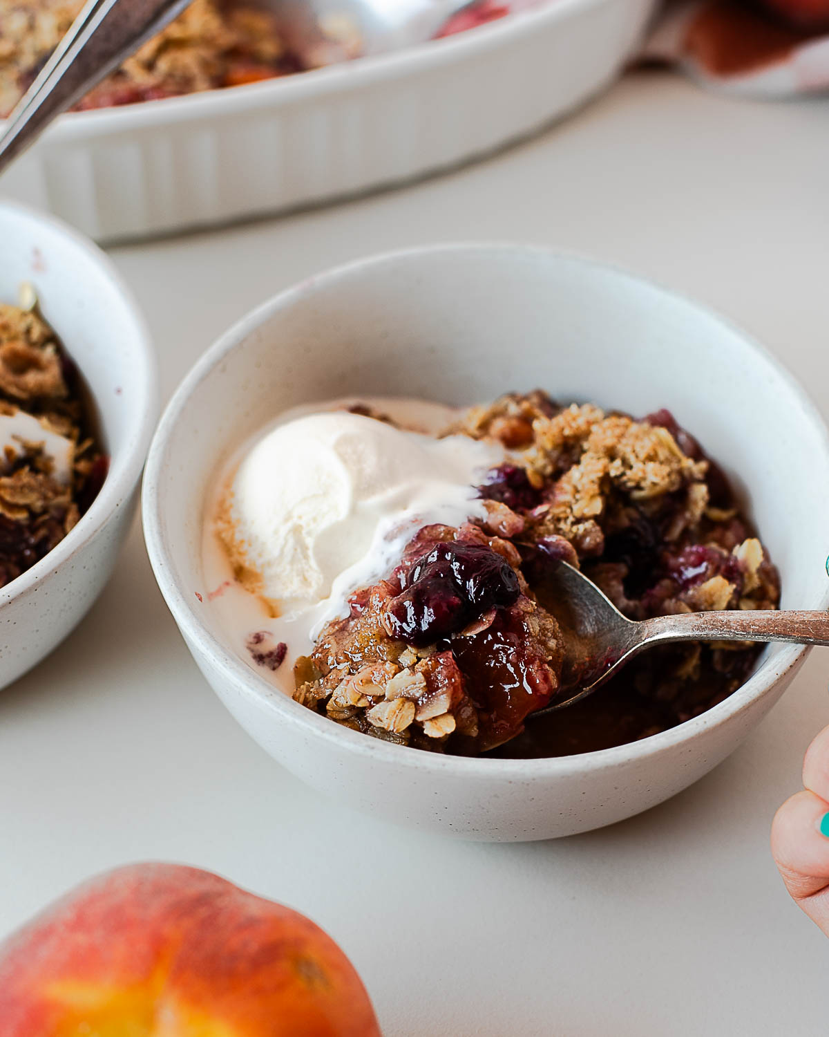 Spoonful of juicy blueberry-peach filling with crunchy oats and ice cream.