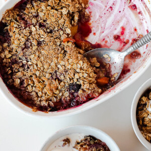 Overhead of half-eaten blueberry peach crisp and two bowls ready to serve.