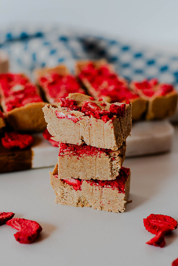 stack of PB&J protein fudge squares on a cutting board with freeze-dried strawberries scattered around.
