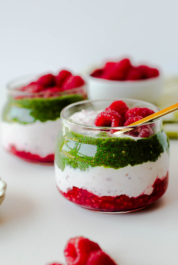 Stunning raspberry overnight oats and matcha chia pudding parfait showing distinct green, white, and red layers.