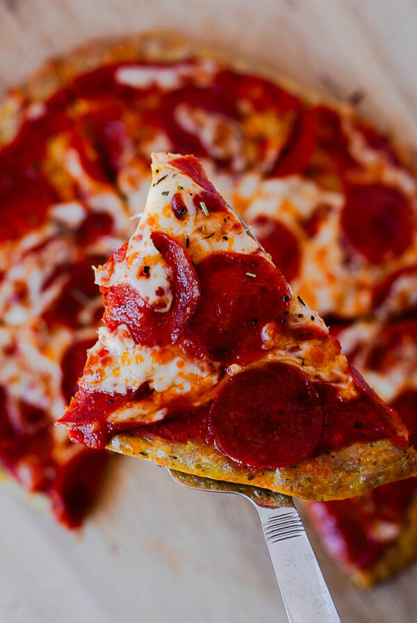 Slice of pepperoni chicken crust pizza lifted from the pizza board with melted mozzarella and pepperoni.